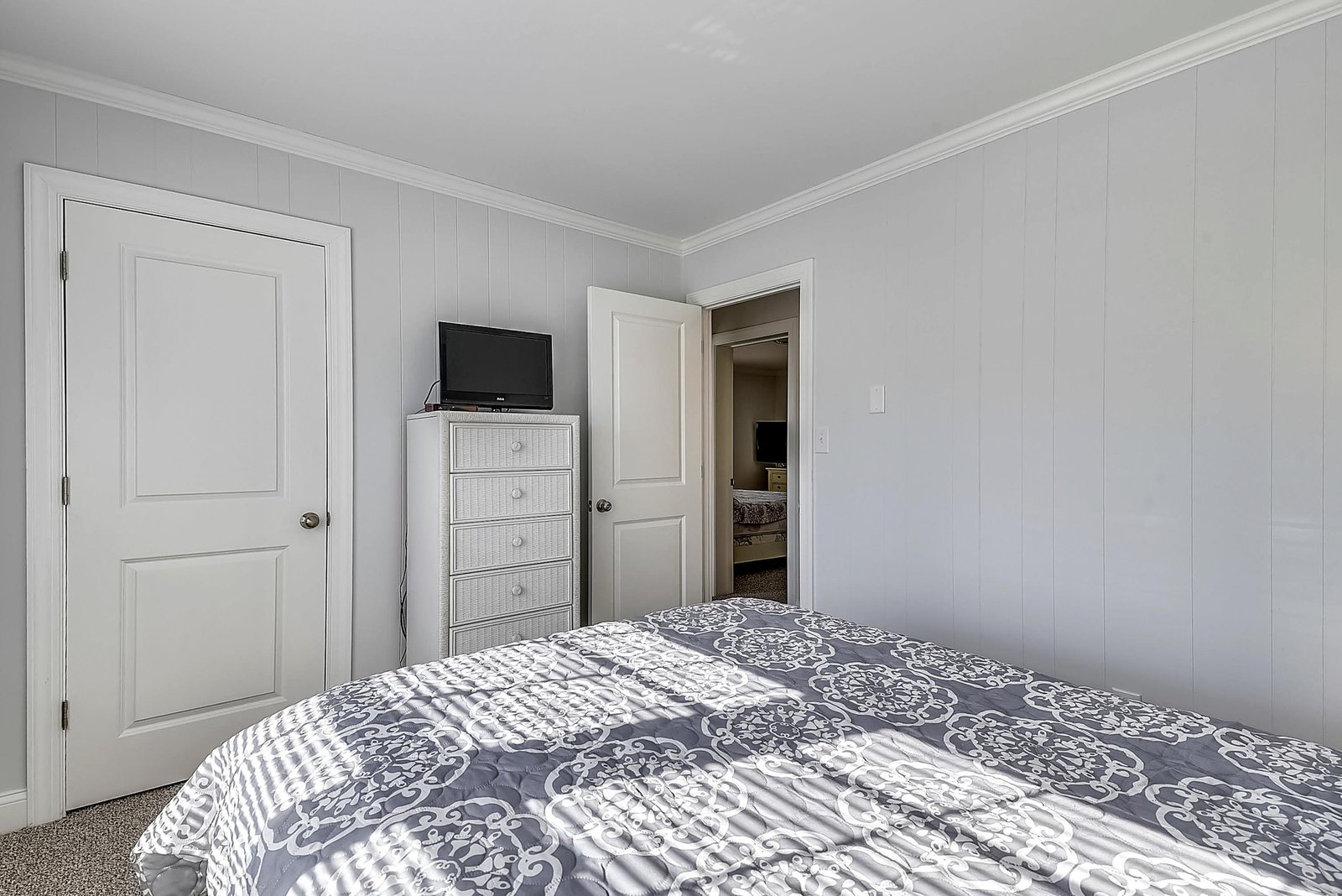 Retreat to your peaceful bedroom with soft linens, bright paneling, and thoughtful coastal touches like the wicker chest—your personal haven for restful nights.