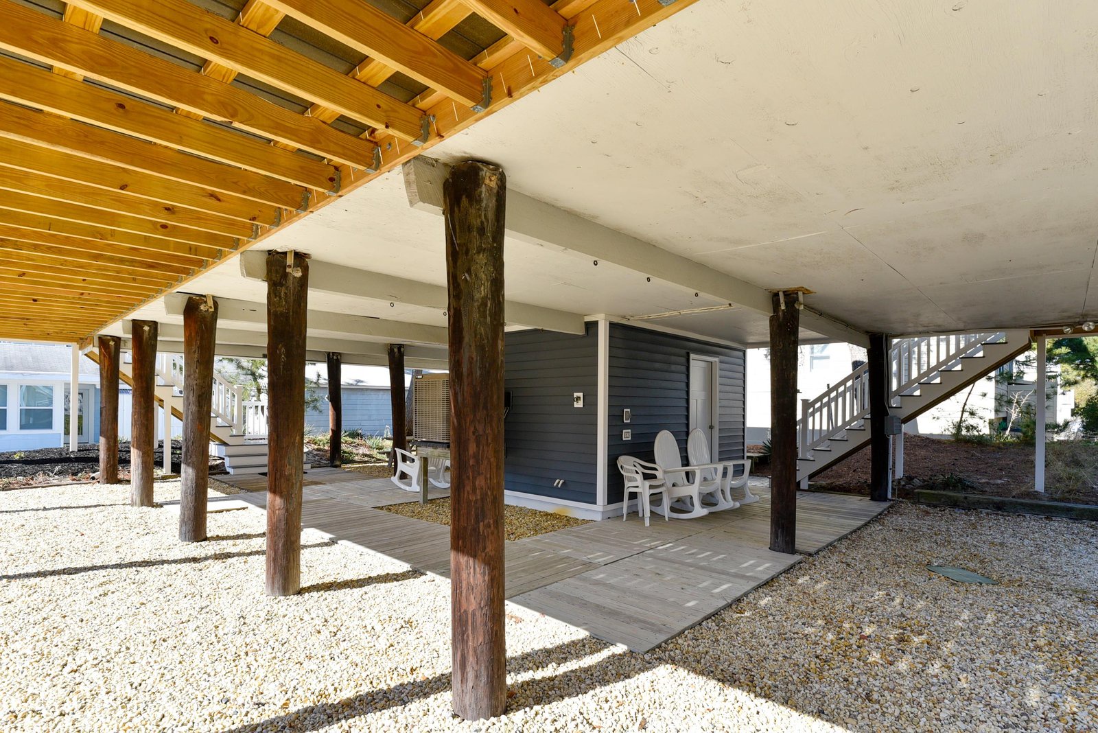 The property features a covered lower level with sturdy timber support posts and gravel ground cover, providing ample space beneath the main structure.
