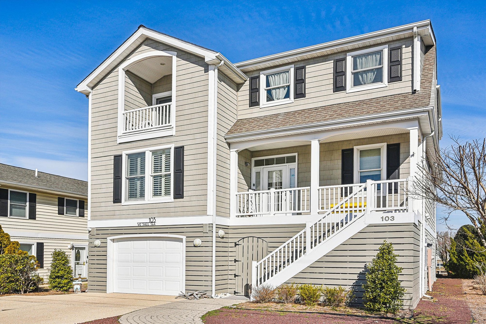Modern coastal home with charming covered porch and welcoming entrance stairs in peaceful residential neighborhood.