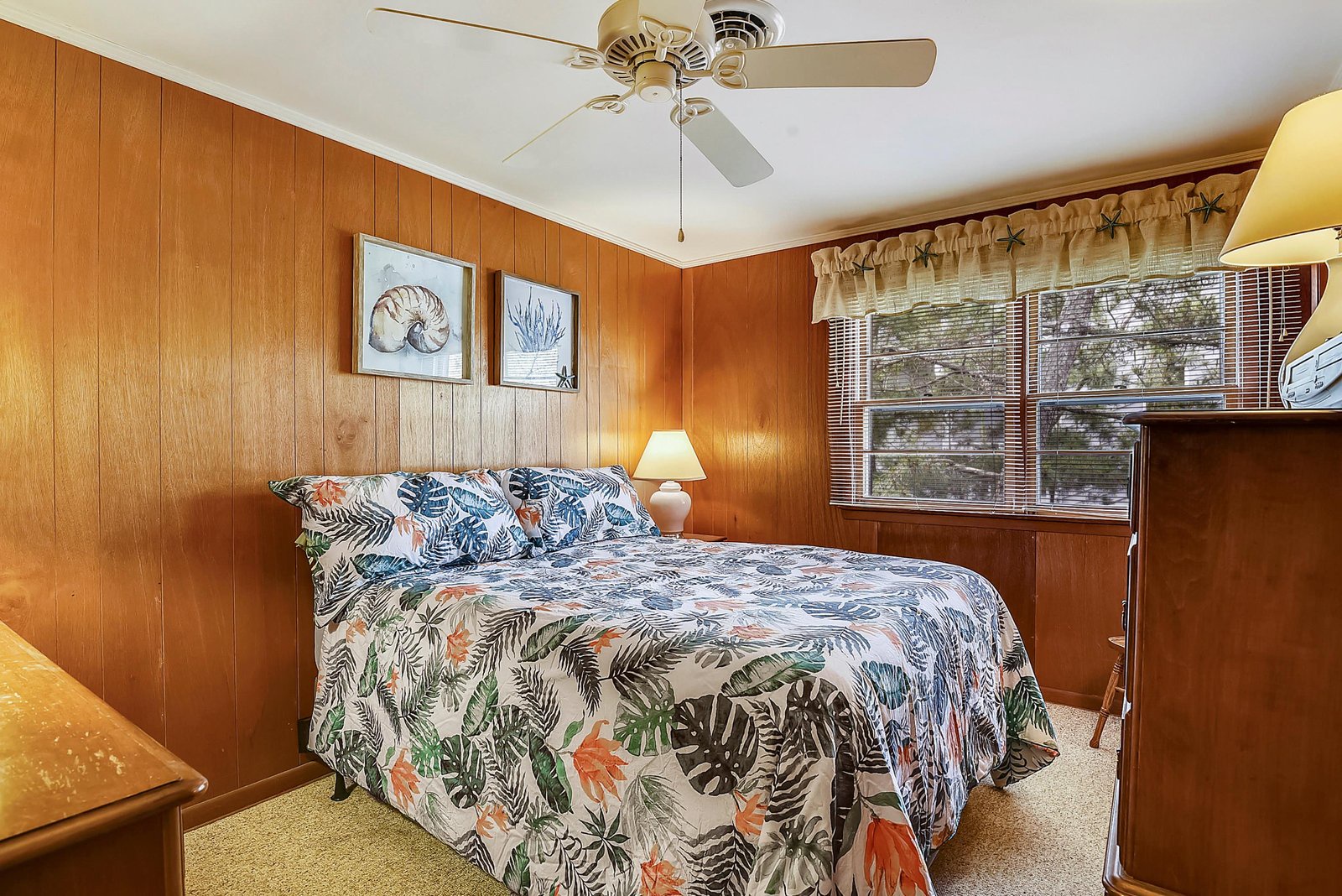 Settle into this cozy bedroom with its warm wood paneling and tropical-themed bedding. Natural light filters through the windows while a ceiling fan keeps you comfortable during your stay.