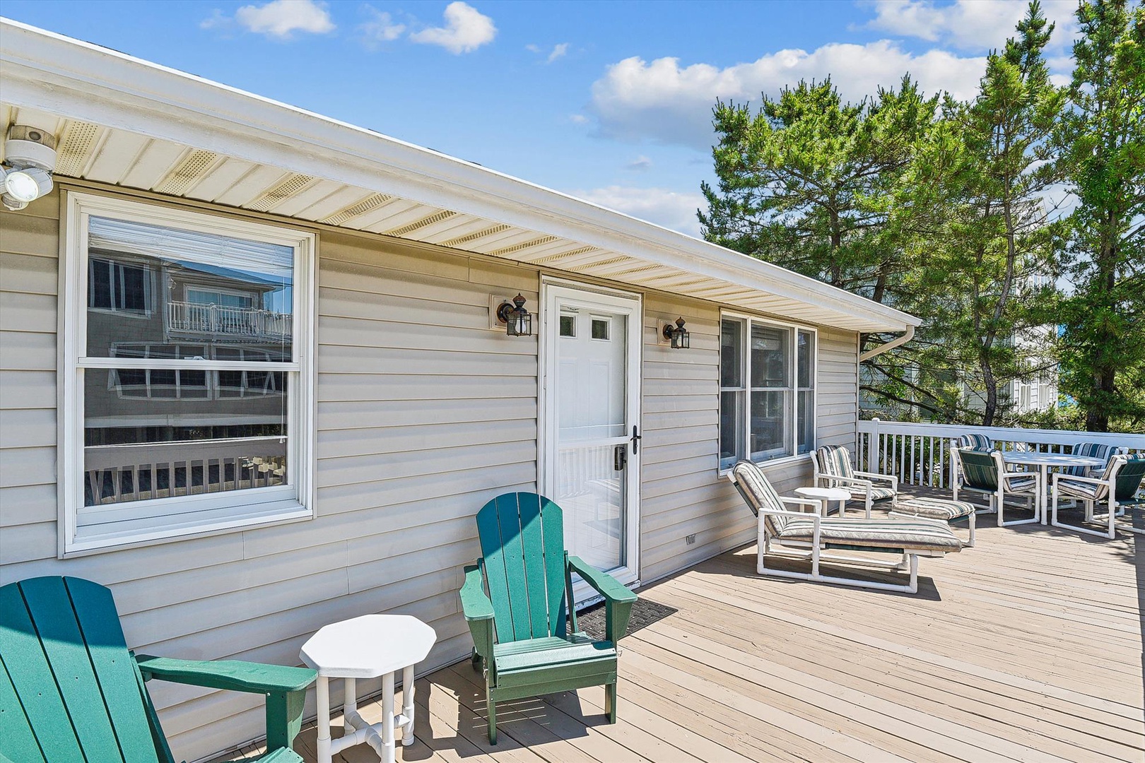 A spacious deck offering multiple seating areas perfect for morning coffee or sunset gatherings. The property is surrounded by tall pines, creating a peaceful retreat setting.