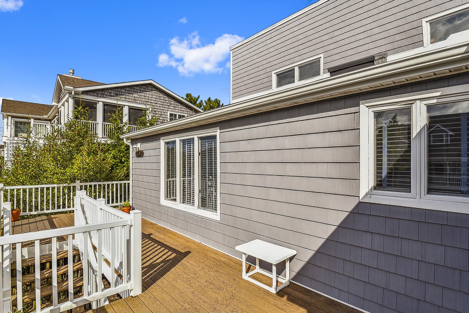 Sunny wooden deck with white railings and bench seating perfect for morning coffee or evening relaxation in a peaceful neighborhood setting.