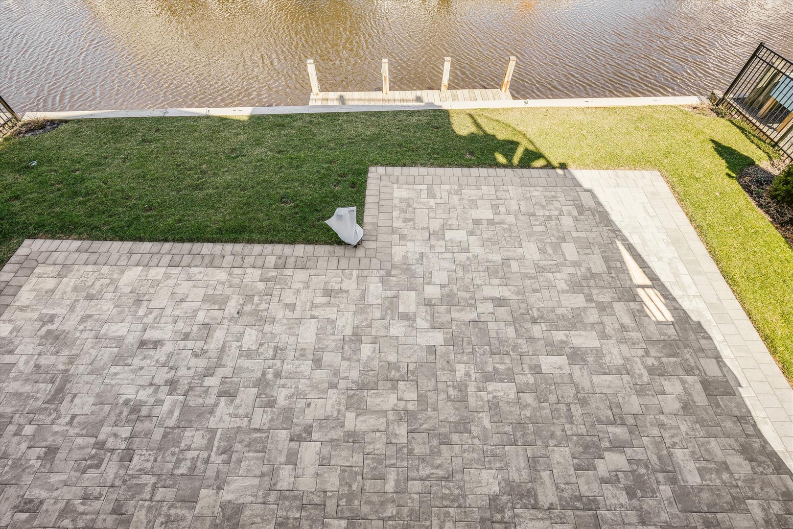 Aerial view captures the property's waterfront setting with a private dock extending over calm waters, surrounded by a spacious lawn and paved patio area.