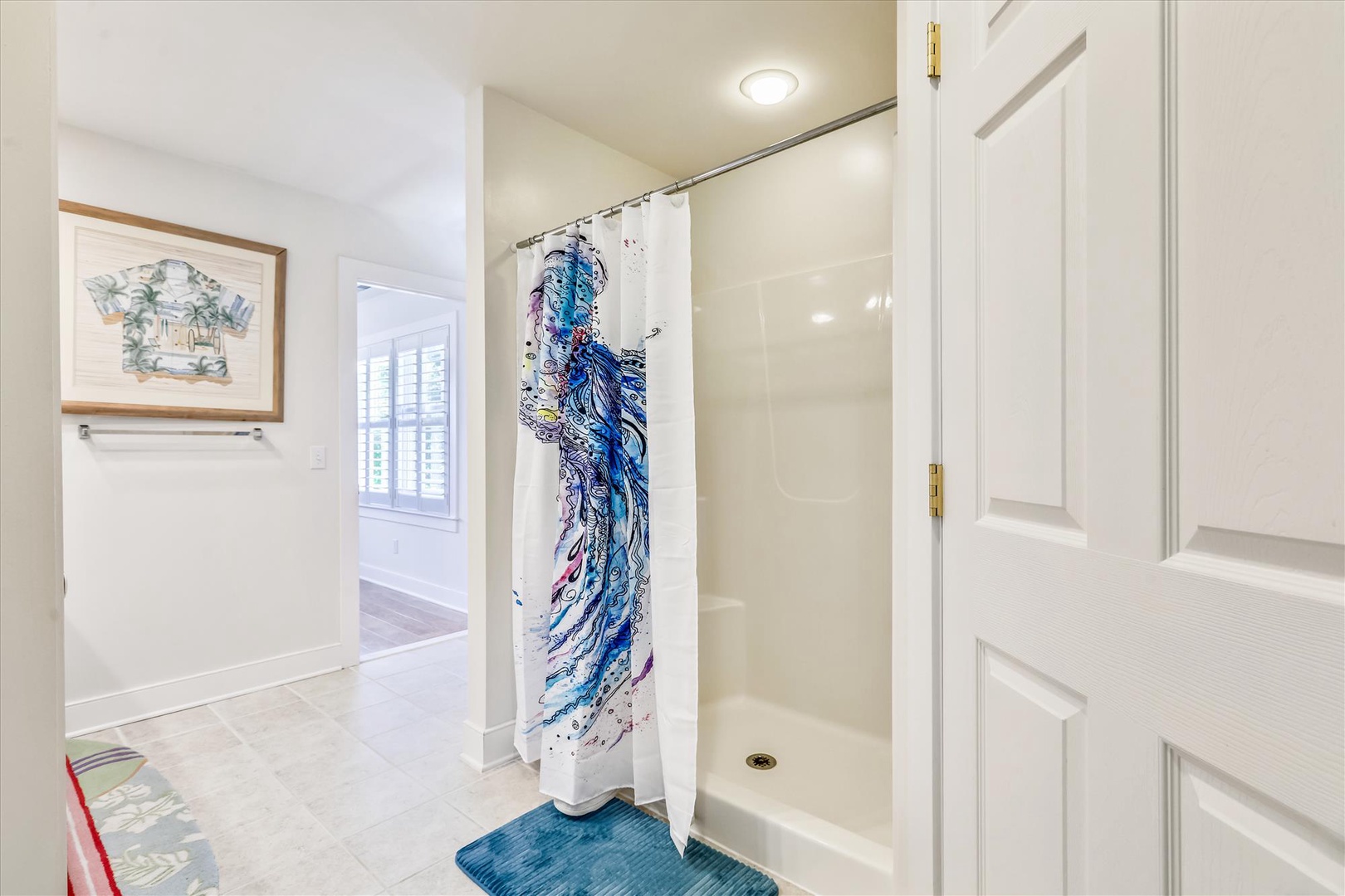 Step into your refreshed ensuite bathroom where coastal vibes meet comfort, featuring a spacious walk-in shower with vibrant artistic touches and soft tile flooring underfoot.