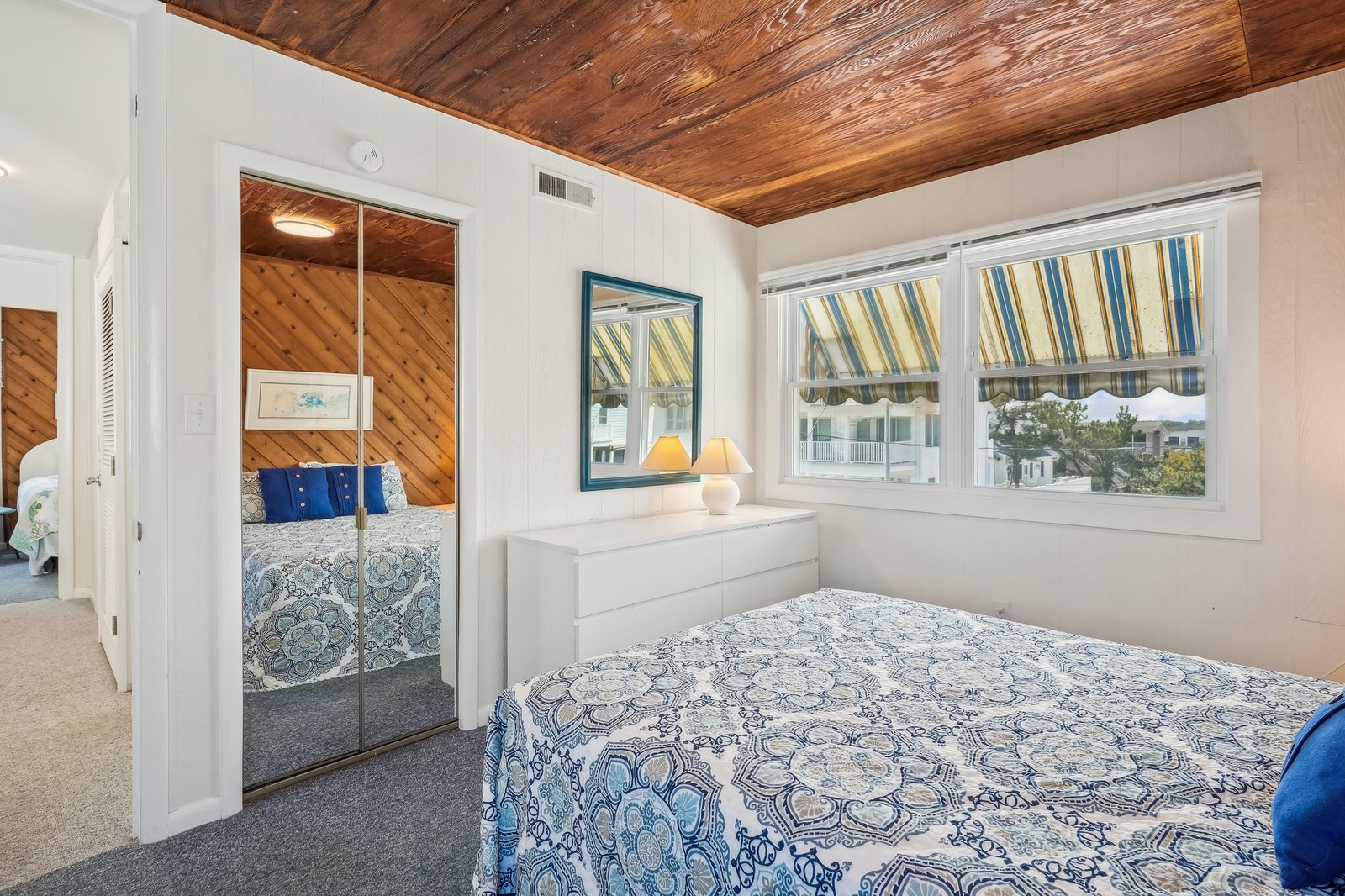 Relax in this charming bedroom with a gorgeous wood-paneled ceiling and large windows dressed in coastal stripes. Your restful retreat opens to an adjoining bedroom, perfect for families or friends traveling together.