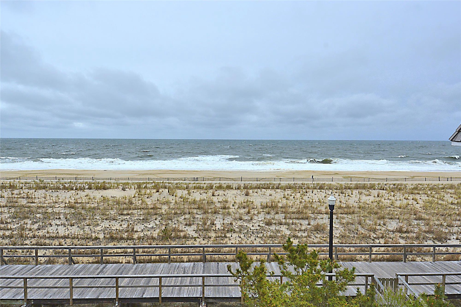 The property features direct beach access with ocean views. Sandy dunes and natural coastal landscape stretch toward the shoreline under an expansive coastal sky.