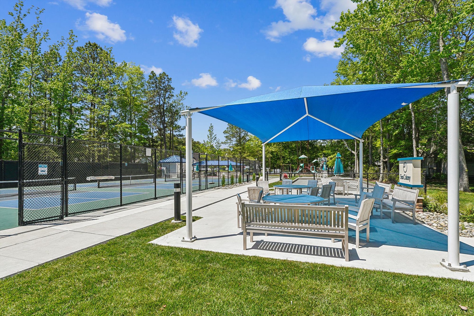 Shaded poolside seating area with tennis courts and mature trees, perfect for outdoor recreation.