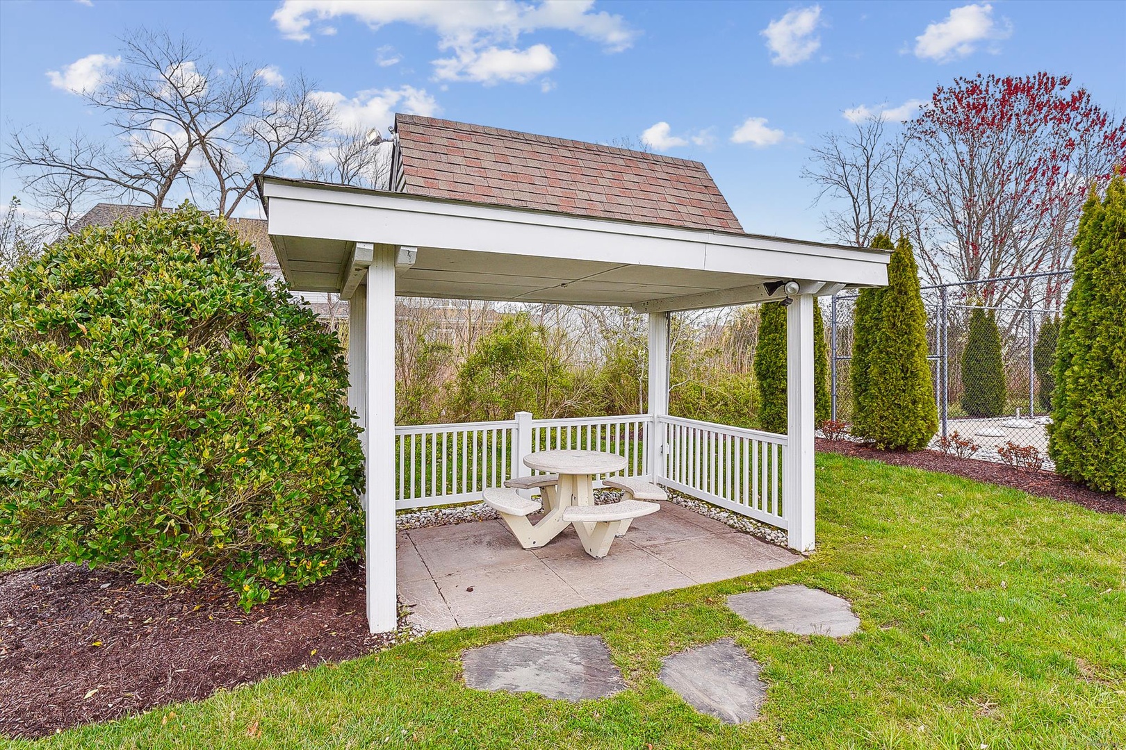 Charming gazebo with a picnic table sits within the property's landscaped grounds, surrounded by mature trees and manicured greenery—a quiet retreat for outdoor relaxation.