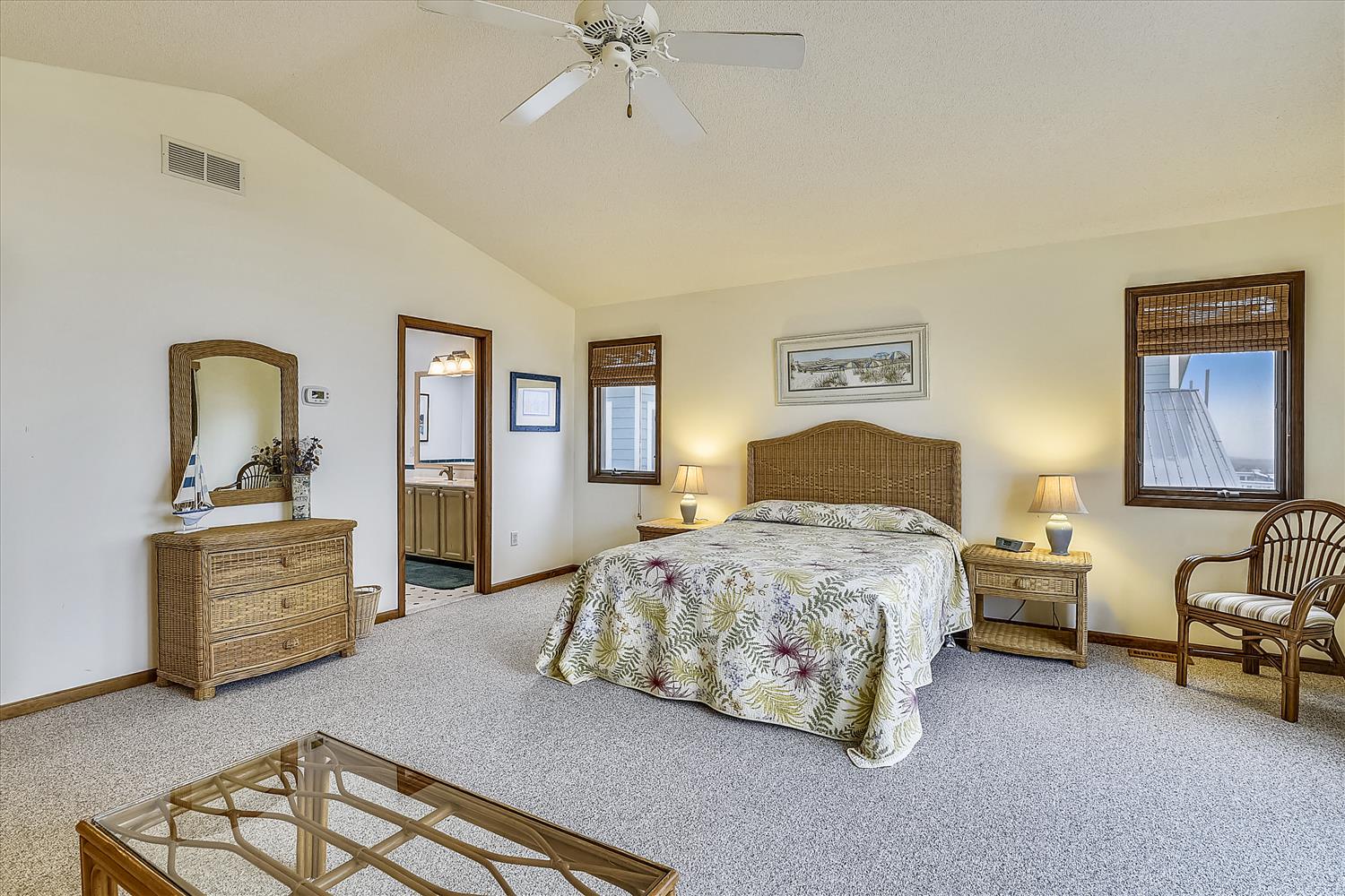 Relax in your spacious bedroom featuring wicker furnishings, tropical bedding, and natural light streaming through bamboo shades.
