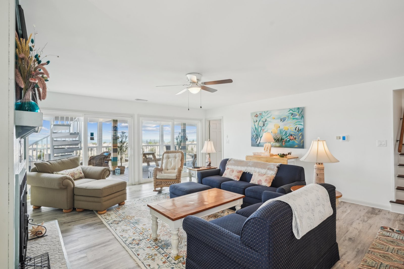 Settle into plush seating as natural light floods this welcoming space through wide glass doors, where coastal breezes and open skies become part of your daily retreat.