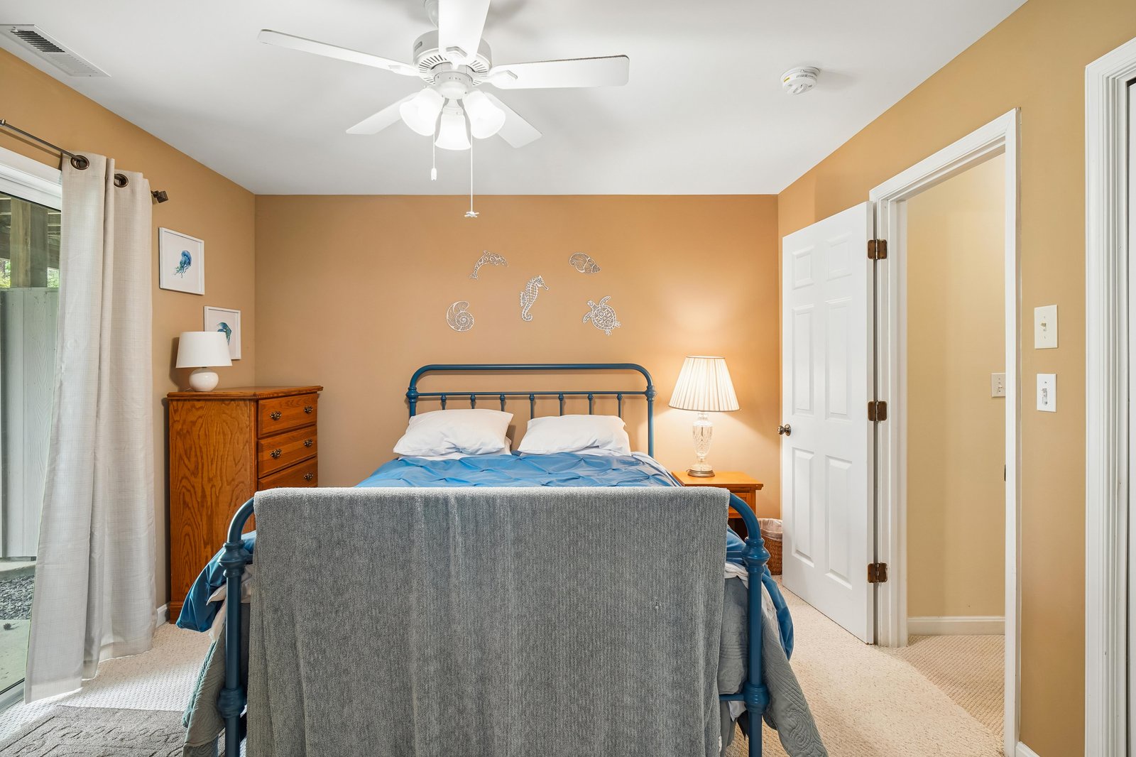 Unwind in your cheerful coastal-themed bedroom, with a comfy bed beneath a ceiling fan and gentle natural light filtering through the curtains.