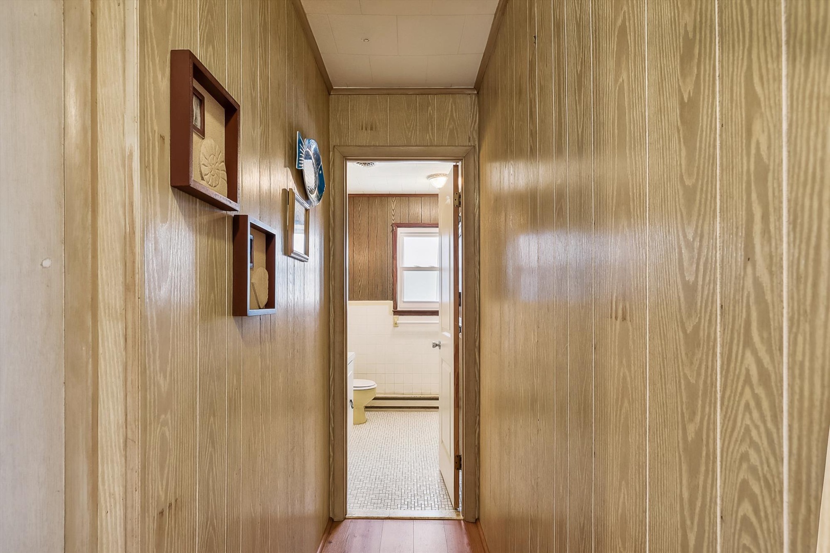 A cozy hallway with warm wood paneling leads to your private bathroom, where natural light and vintage charm create a welcoming retreat.