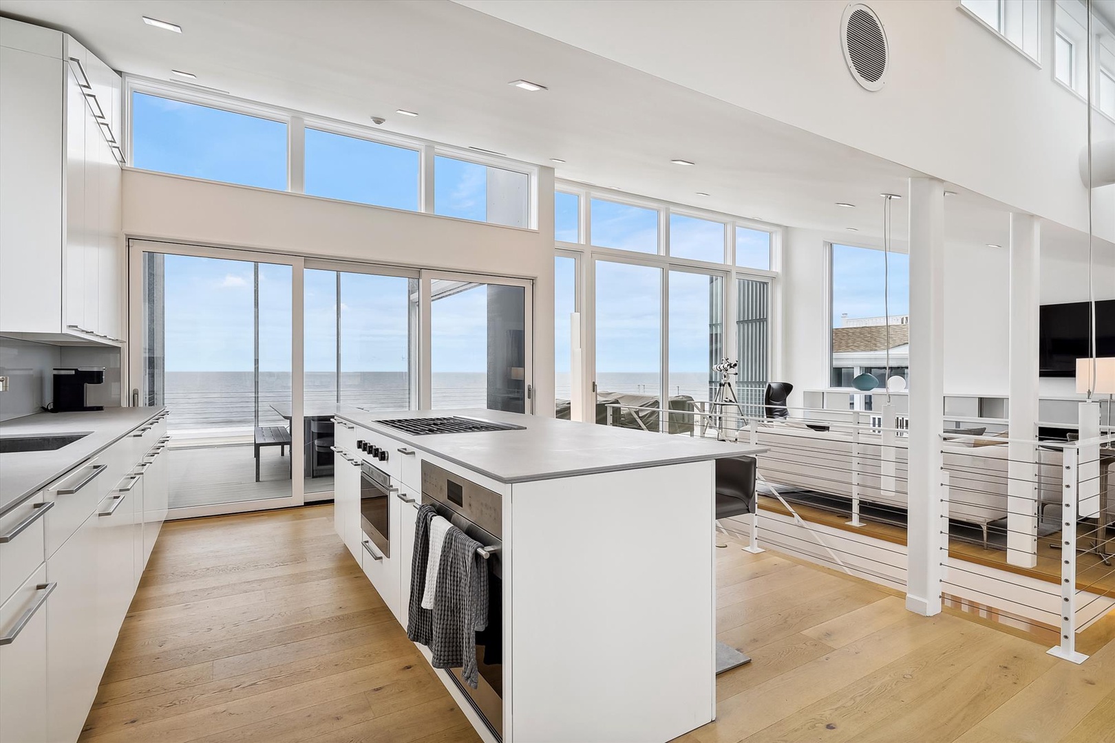 Sunlit, airy kitchen opens to a breathtaking sea view. Imagine preparing meals at the sleek island while the ocean stretches before you, blending effortless coastal living with modern comfort.
