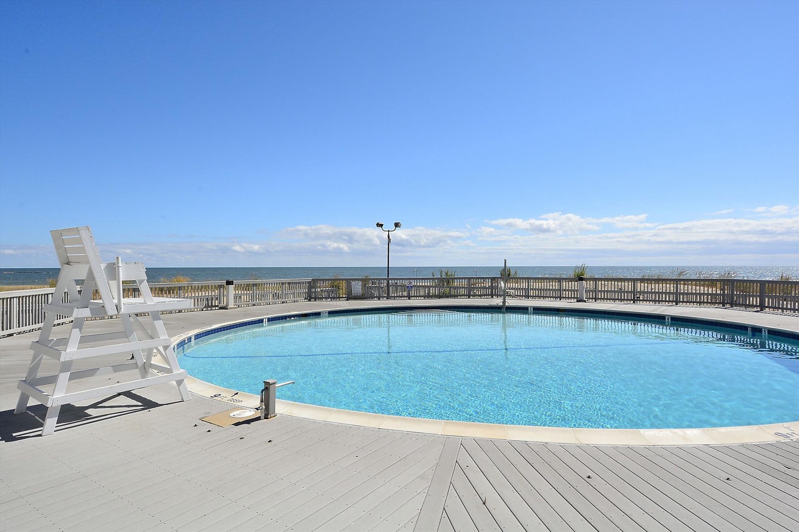 Sparkling beachfront pool with white lounge chairs awaits, offering refreshing swims and stunning ocean views beyond the deck railing.