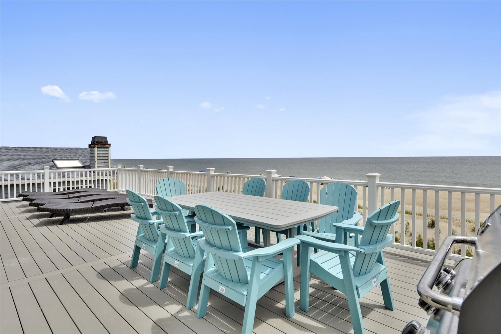 Expansive deck with turquoise Adirondack chairs and dining table overlooking the ocean, offering panoramic sea views during your stay.