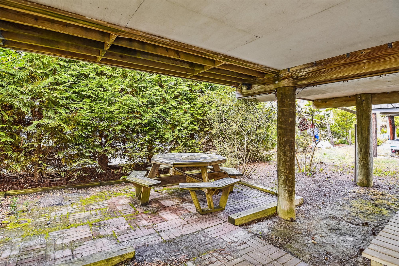 A covered outdoor seating area offering a peaceful spot to relax under shelter. Wooden beams and lush greenery surround this quiet space, perfect for enjoying fresh air.