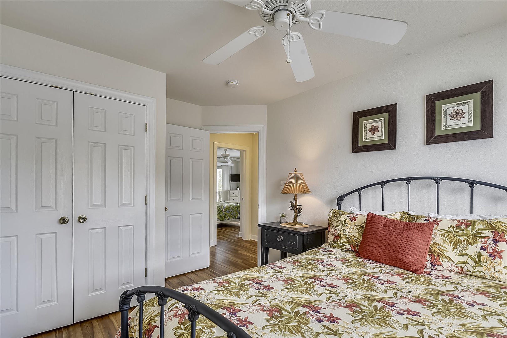 Step into your cozy retreat with a comfortable bed dressed in inviting floral linens, a gentle ceiling fan overhead, and warm wood floors underfoot.