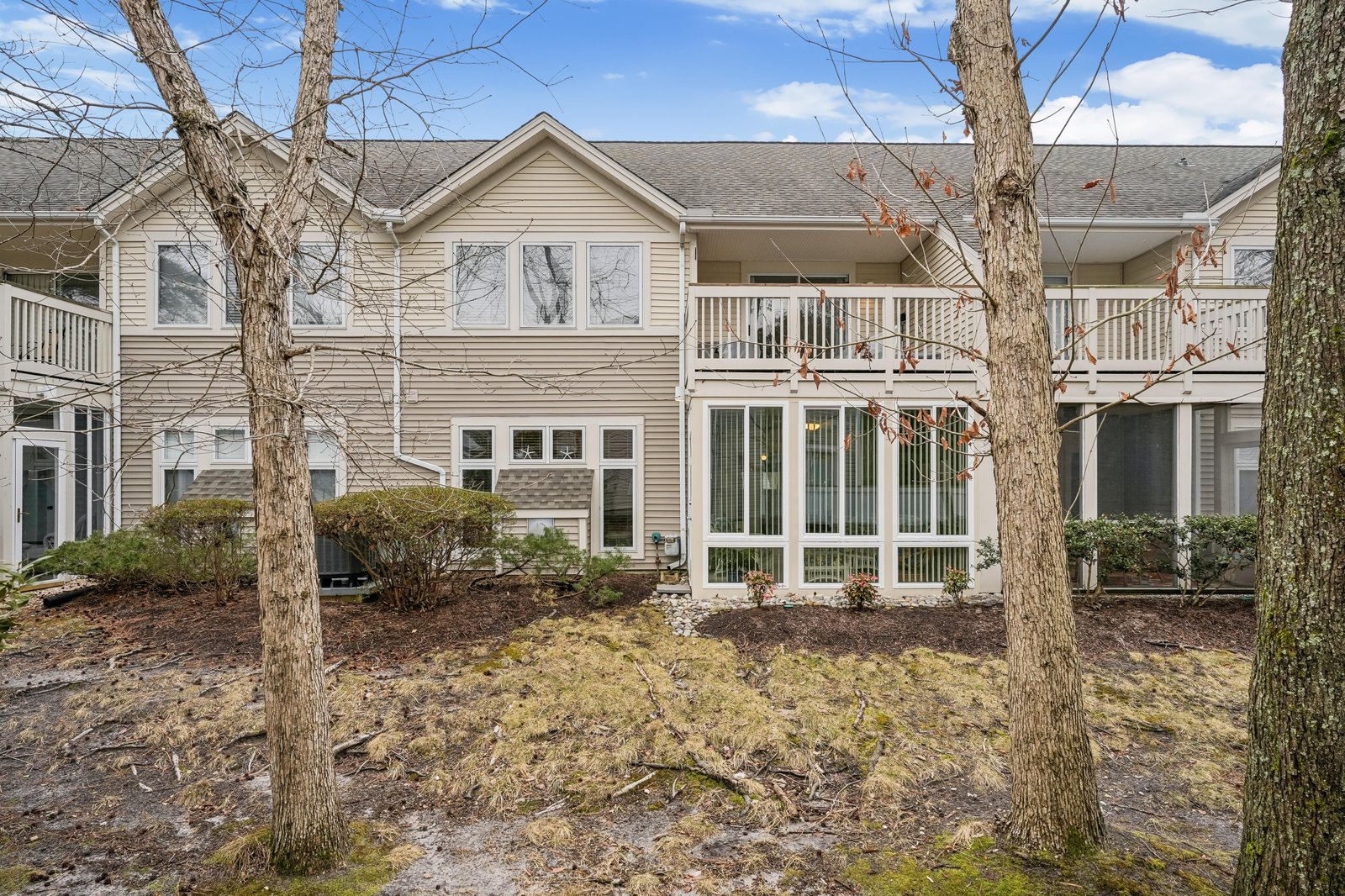 A welcoming two-story vacation retreat featuring dual balconies and expansive windows, framed by mature trees and surrounded by peaceful natural landscaping perfect for your getaway.