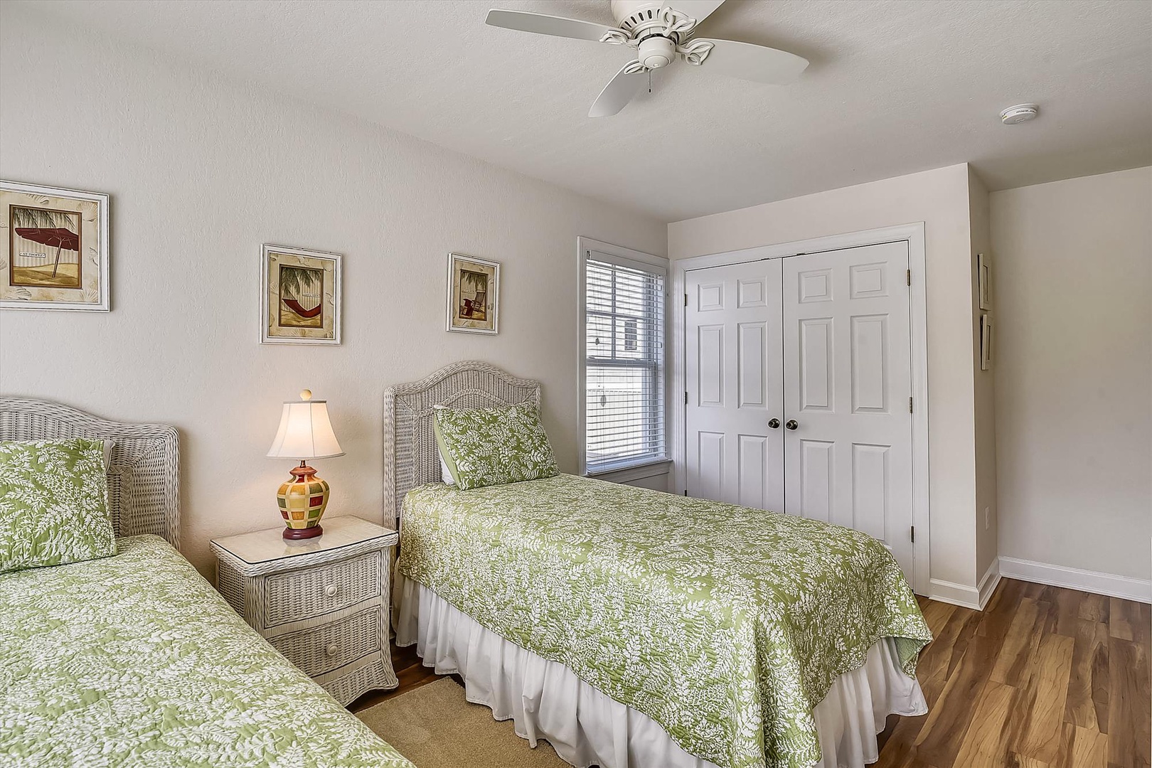 Your charming twin bedroom awaits with plush green bedding, natural wicker accents, and gentle ceiling fan creating perfect coastal comfort for restful nights.