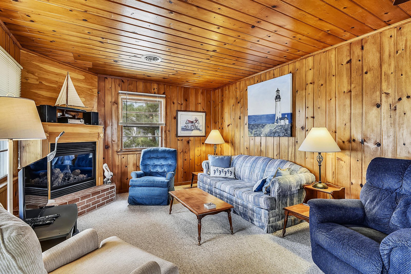 Sink into soft cushions beside the glowing fireplace in this warm, wood-paneled living room. Your cozy coastal escape awaits with plenty of comfortable seating for relaxation.