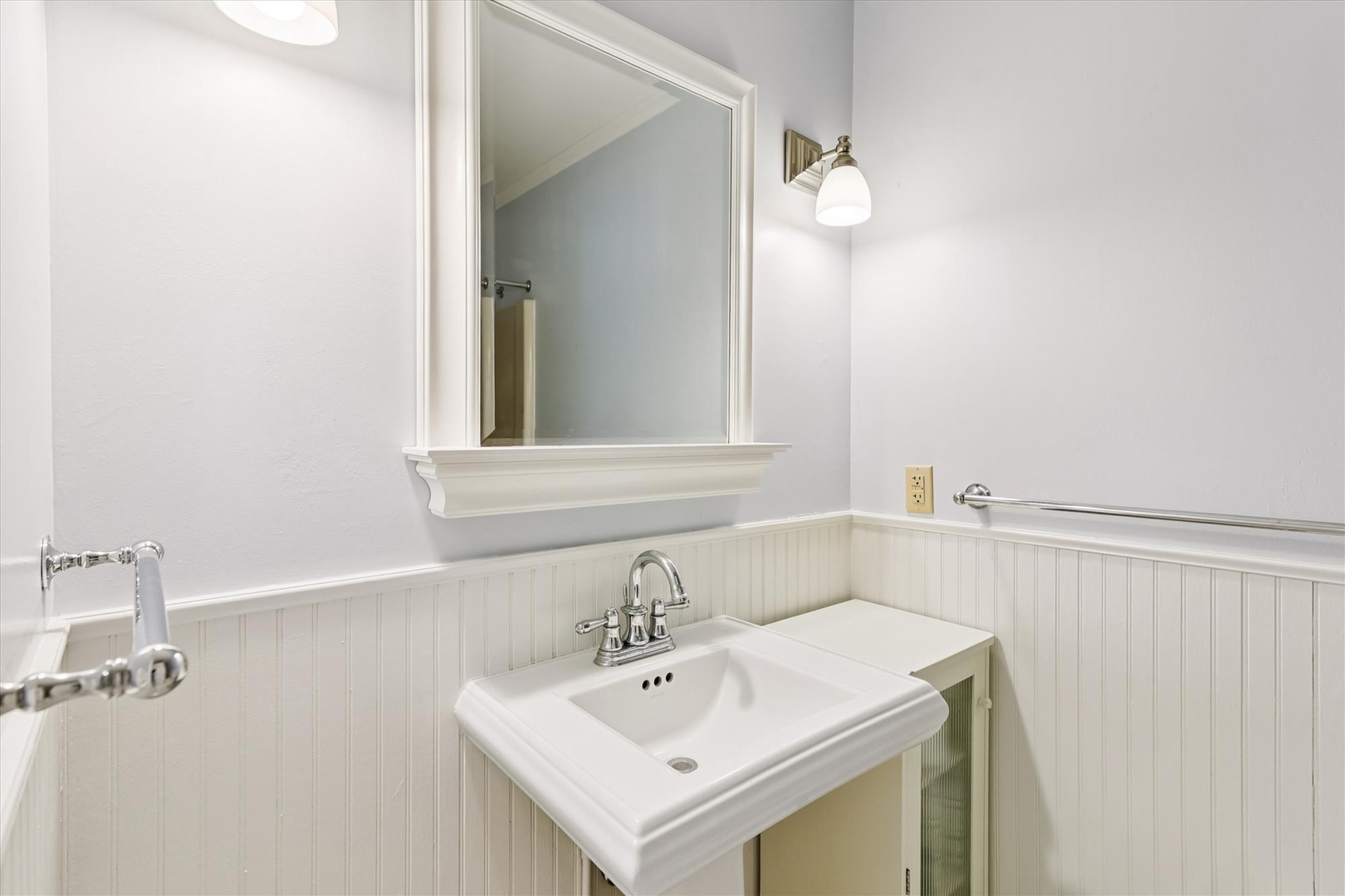 Step into your pristine bathroom featuring classic white beadboard wainscoting and elegant fixtures for your comfort.
