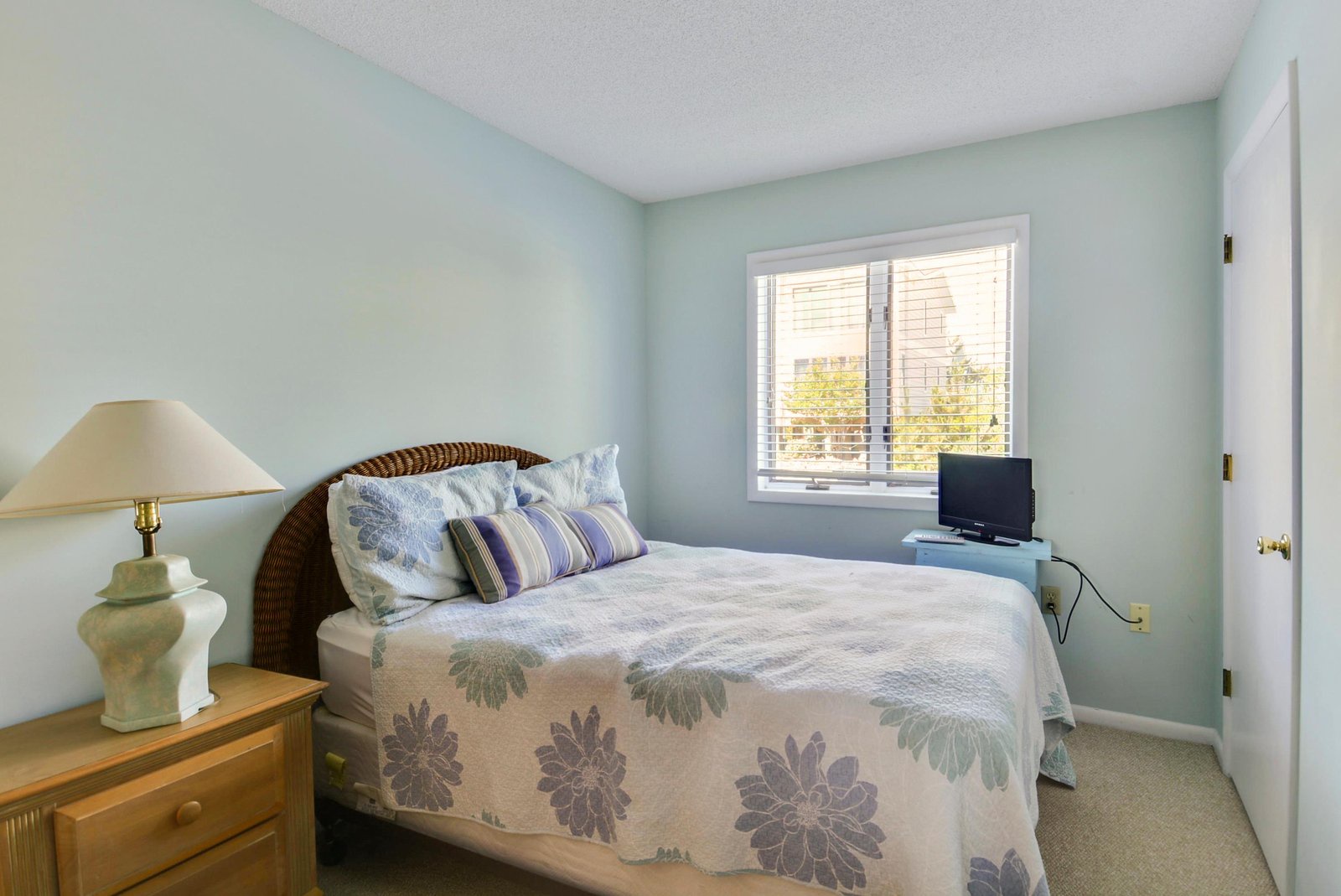 Your peaceful sanctuary awaits with soft coastal hues and natural light streaming through the window, offering restful views of the neighborhood greenery.
