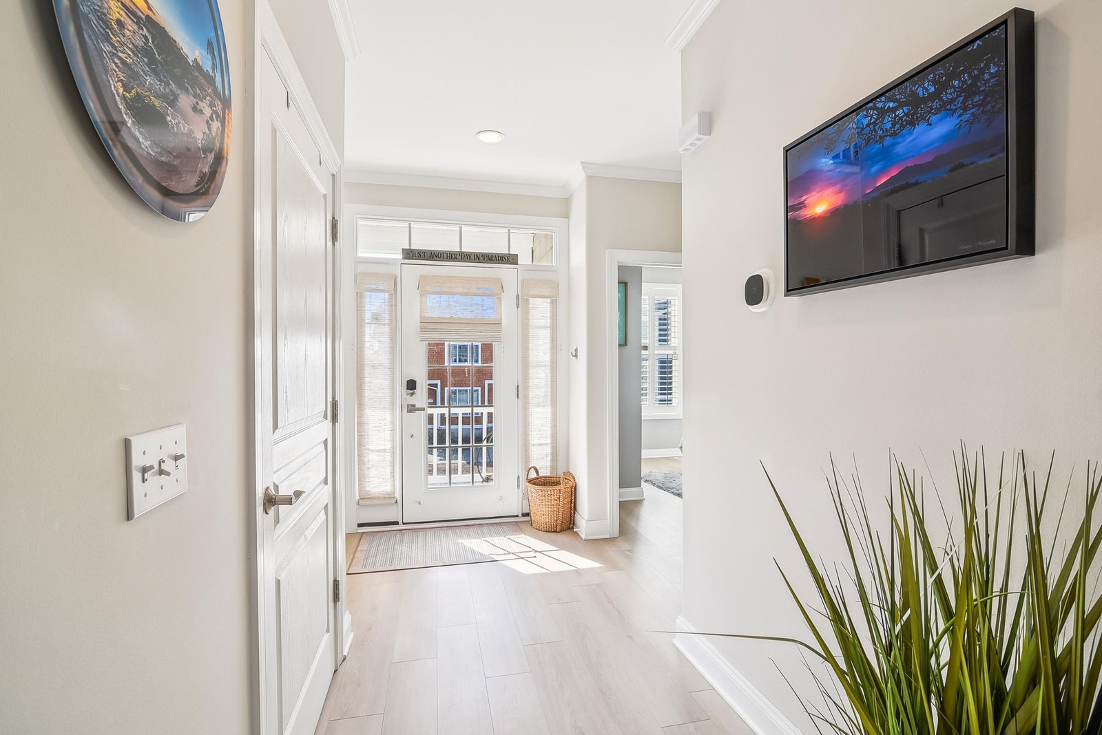 A bright entryway welcomes you home with crisp white details and natural light streaming through the glass door. Fresh greenery adds a serene touch to the elegant, open foyer.