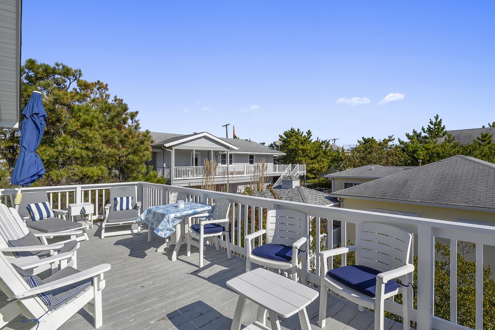 A spacious rooftop deck overlooks the surrounding neighborhood, featuring dining and lounging areas perfect for sunny gatherings with blue coastal skies above.