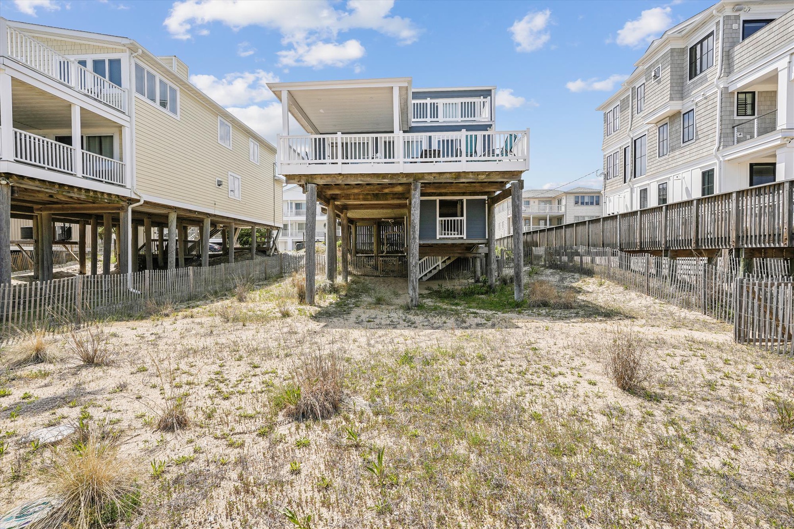 Elevated beachfront home with direct sandy access, featuring covered ground-level parking and spacious upper-deck balconies overlooking the dunes and neighboring beach properties.
