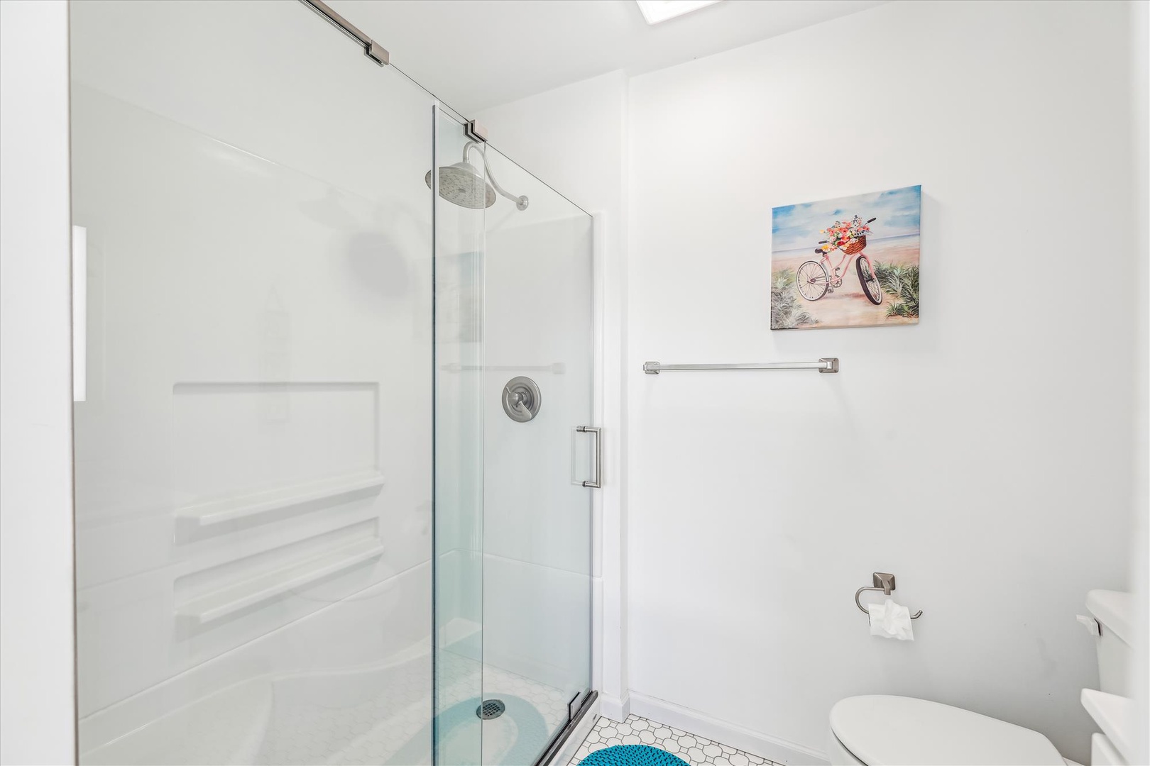 Your private bathroom features a spacious walk-in shower with rainfall showerhead, bright white tile, and cheerful coastal artwork—clean, modern, and ready for you.