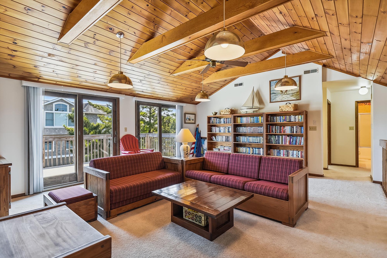 Your cozy living room features vaulted wood ceilings with exposed beams, a plush seating area, and a well-stocked library. Natural light pours through glass doors that open to a private deck with neighborhood views.
