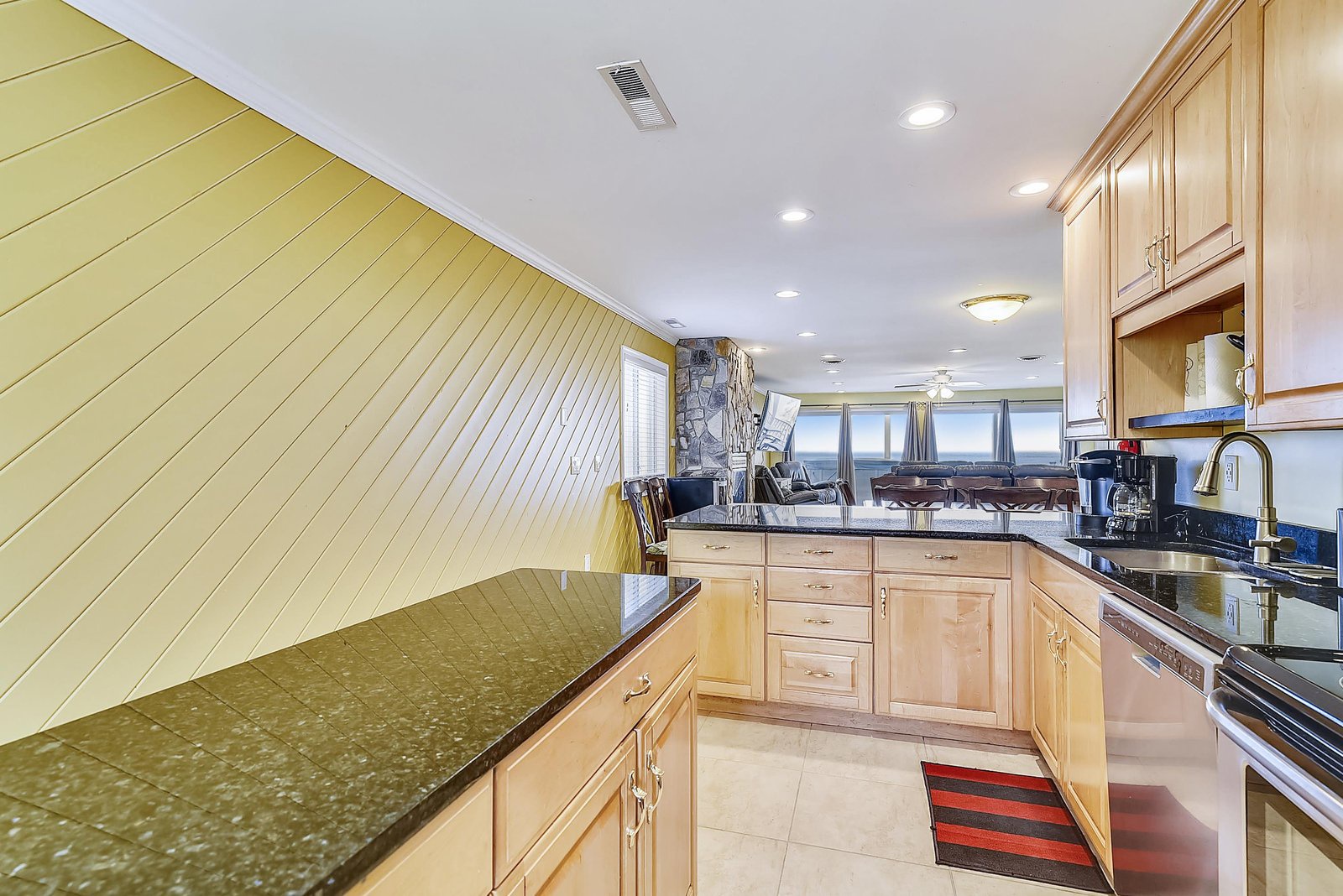 Step into your fully equipped kitchen with granite countertops, natural wood cabinetry, and open views into the cozy living area where sunlight streams through multiple windows.