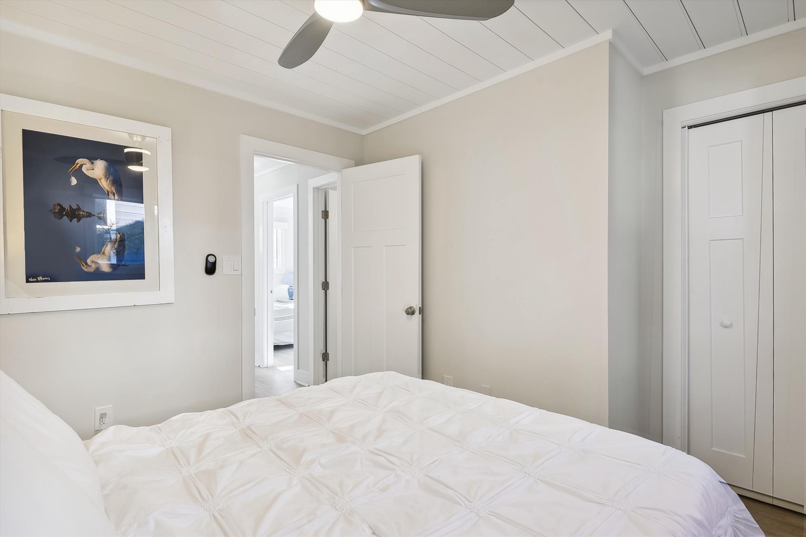 Drift off beneath soft linens and a calming ceiling fan in your peaceful retreat, where crisp white walls and coastal artwork set the tone for restful nights.
