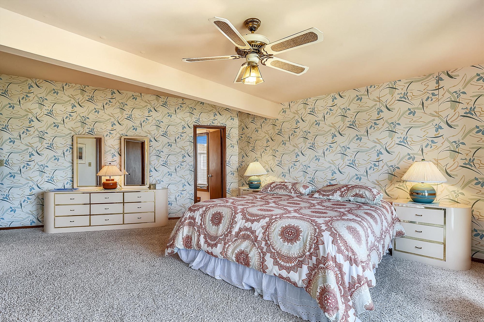 You'll drift into restful sleep in this spacious, bright bedroom featuring soft patterned wallpaper, cozy bedding, and a gentle ceiling fan breeze overhead.