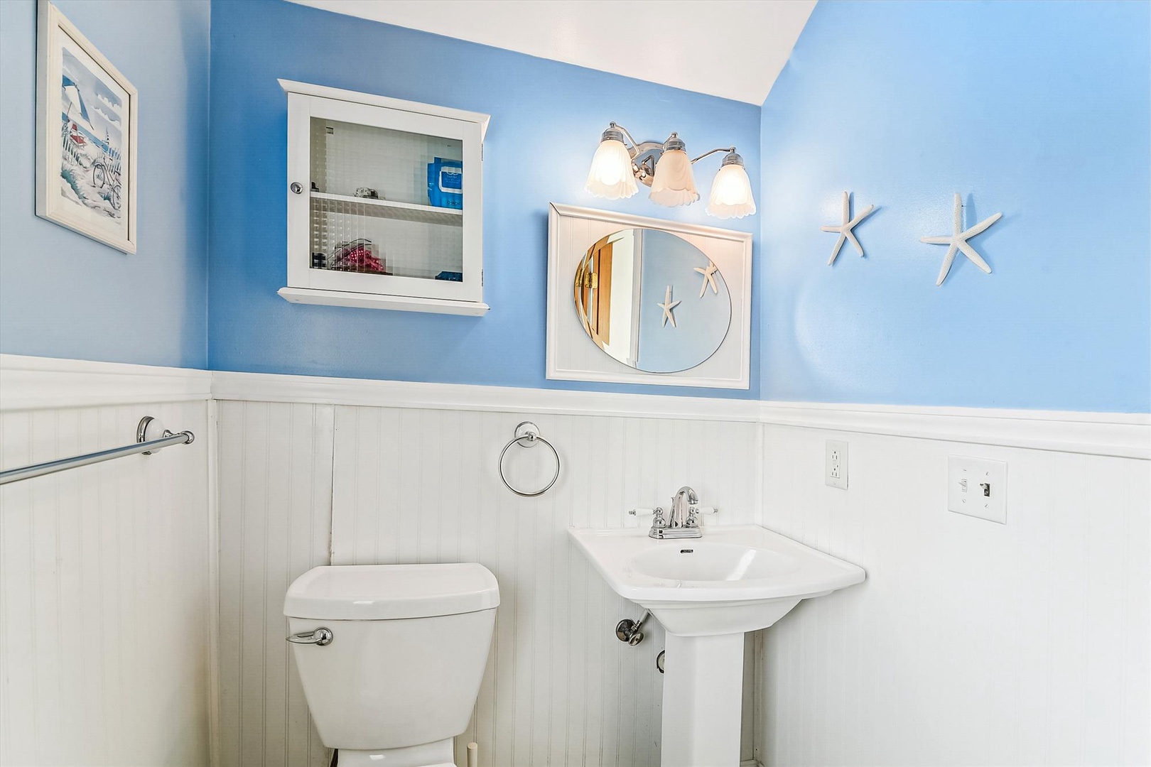 Freshen up in this coastal-inspired bathroom featuring white beadboard wainscoting, soothing blue walls, and charming starfish accents that bring a breezy seaside feel to your stay.