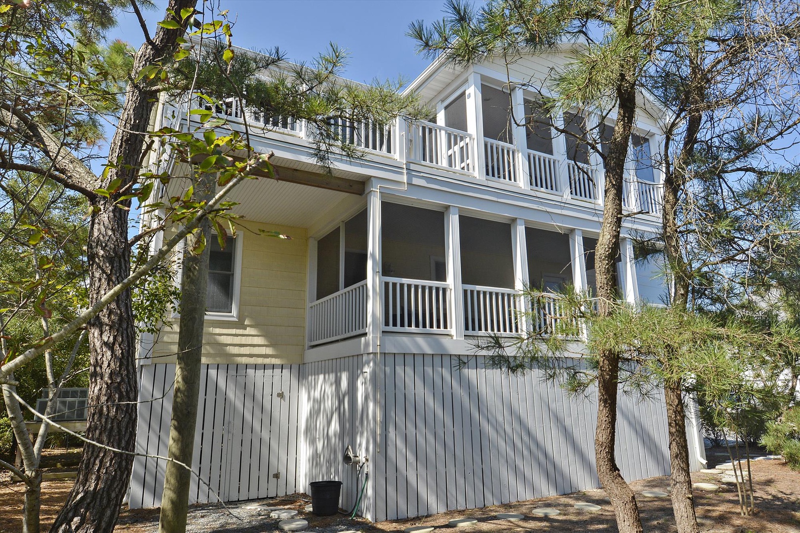 This coastal retreat stands amid tall pines, offering screened porches and balconies on two levels, perfect for enjoying the natural surroundings and sea breeze during your stay.