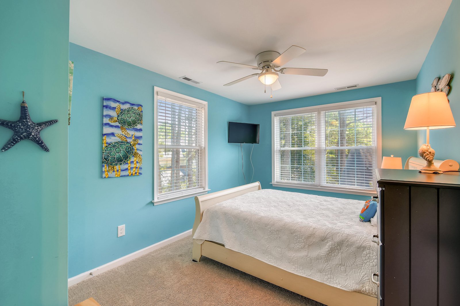 Drift off in your coastal-inspired bedroom, where soothing turquoise walls and natural light from large windows create a serene retreat for restful nights.