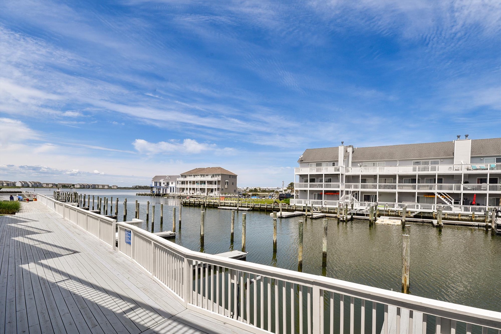 Multi-level waterfront property featuring marina docks and boat slips along calm bay waters, accessible via wooden boardwalk with white railings.