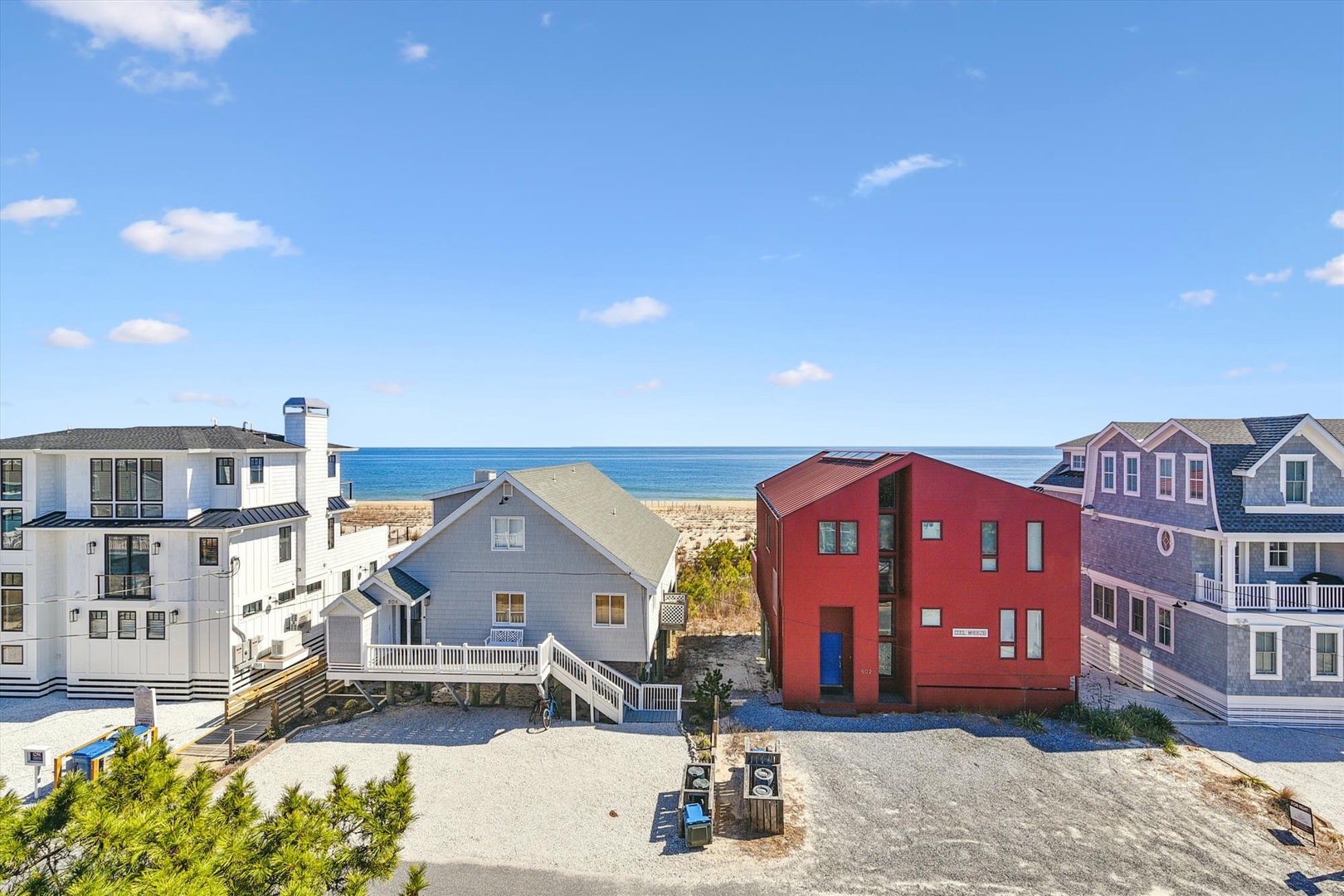 Coastal neighborhood featuring a distinctive red beachfront property with direct ocean access and surrounding beach homes under clear blue skies.