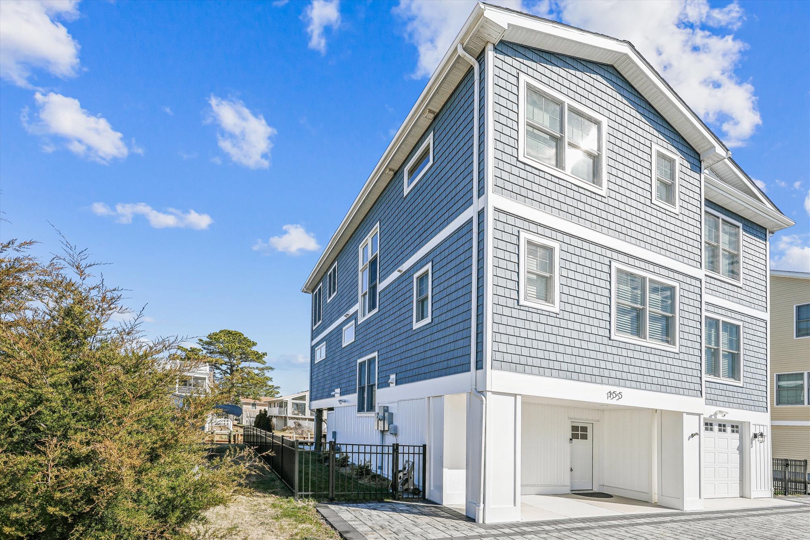 Modern coastal home with distinctive blue shingle siding and spacious garage level, perfectly positioned in a quiet residential neighborhood.