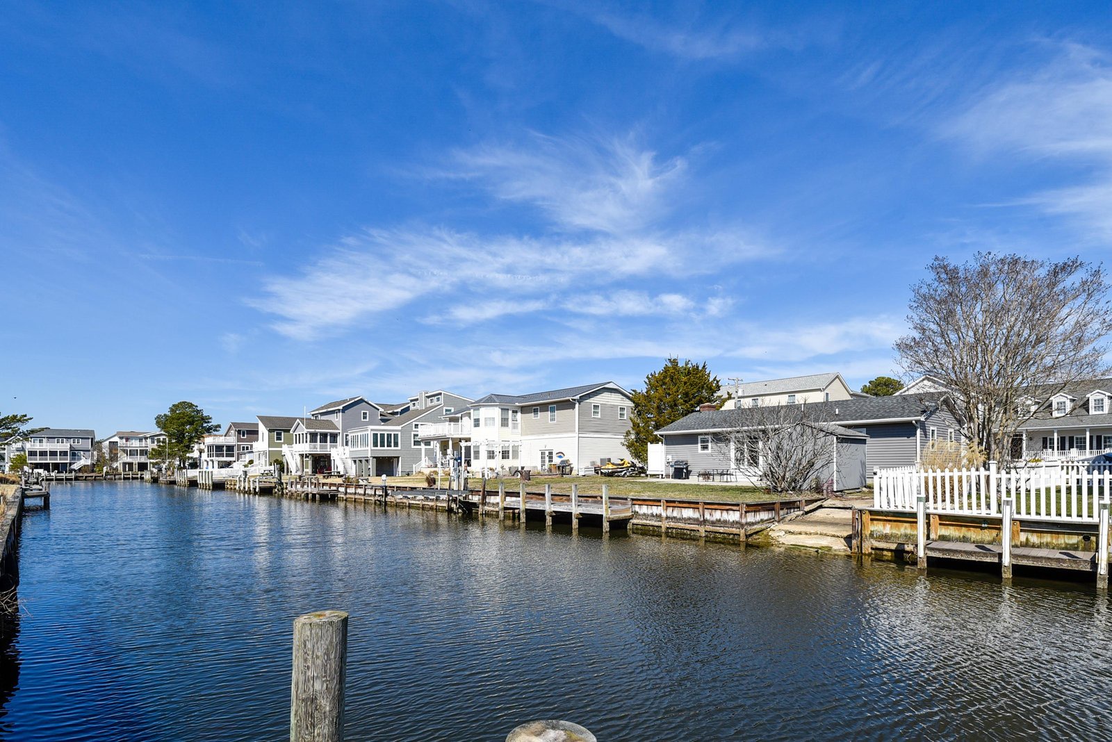 Waterfront homes line a peaceful canal with private docks under a clear blue sky, offering tranquil coastal living just steps from your door.
