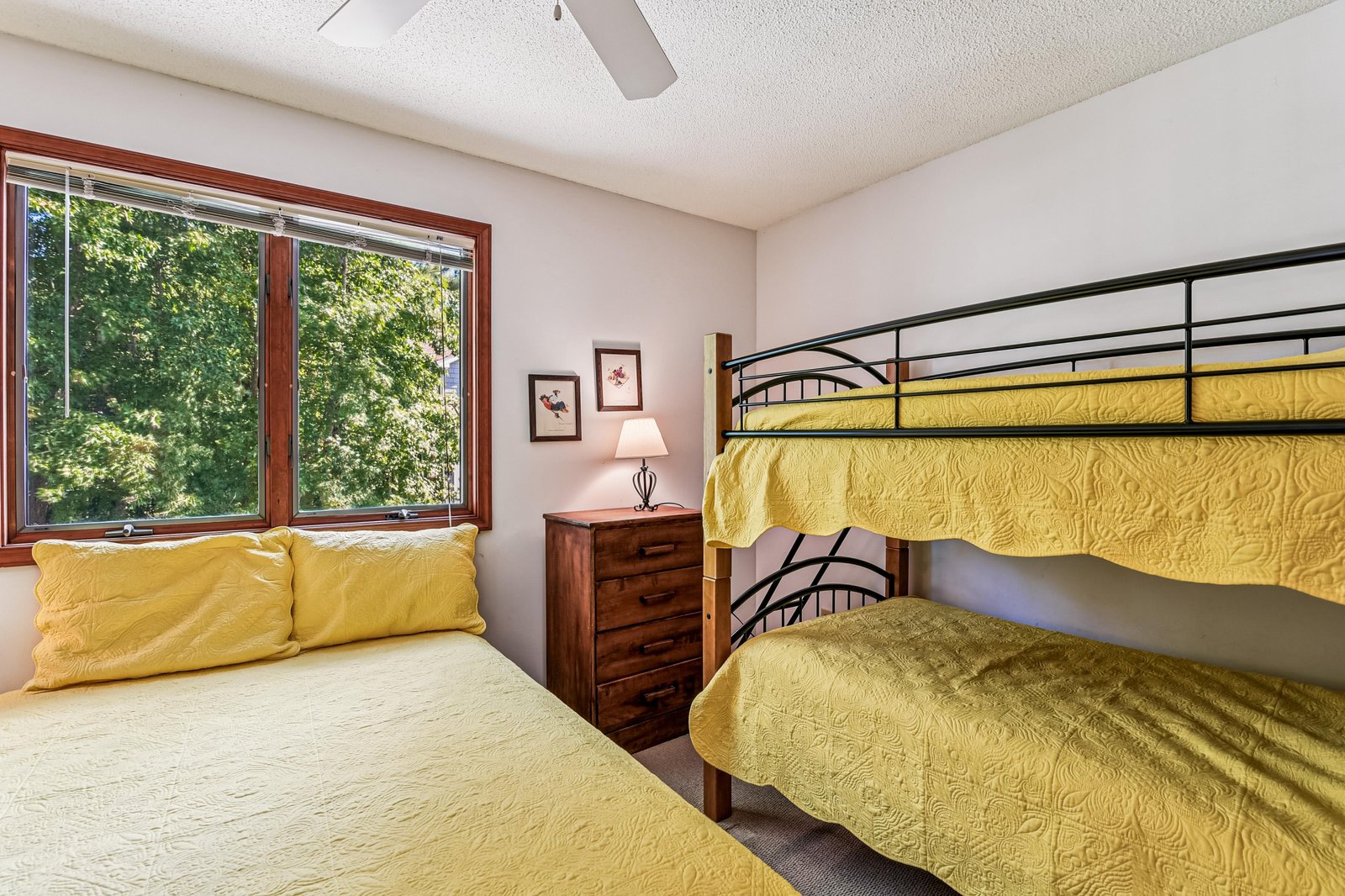 Your cheerful bedroom features sunny yellow linens on a comfy bed and bunk, perfect for families or friends traveling together. Wake up to natural light streaming through the large window, framing a peaceful, leafy view.