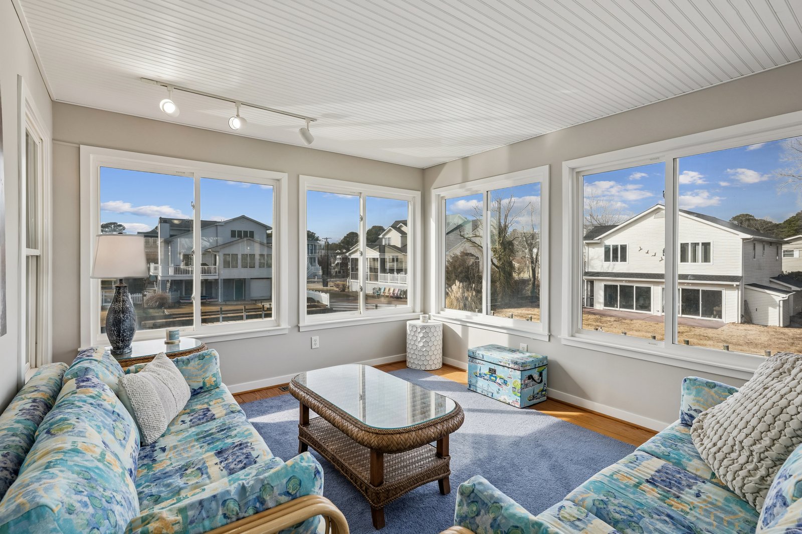 Relax in your bright sunroom with panoramic windows, comfy coastal seating, and charming neighborhood views.