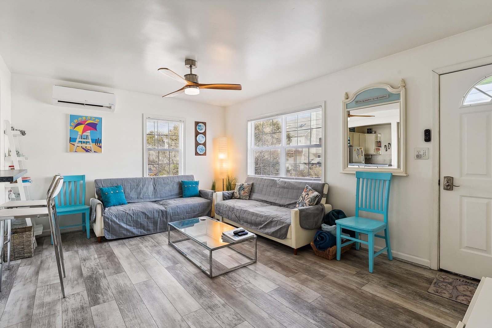 Sink into plush seating and unwind in your bright, airy living space. Coastal charm meets modern comfort with fresh blue accents and natural light streaming through the windows.