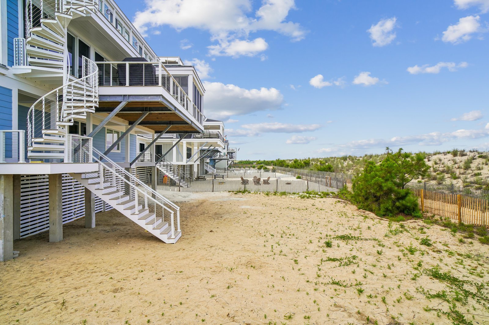 Bright beachfront property set directly on the sand with dune grass and coastal vegetation. Features spacious balconies and exterior stairs for easy beach access.