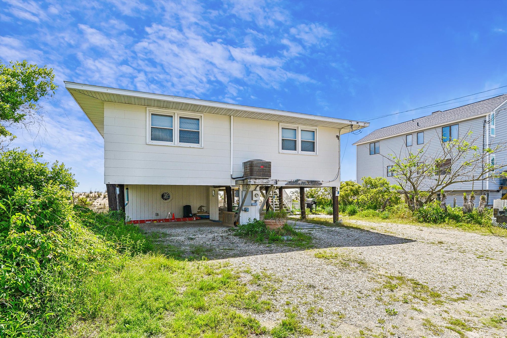 Elevated beach home with covered parking and natural landscaping, situated in a quiet coastal neighborhood near the shore.