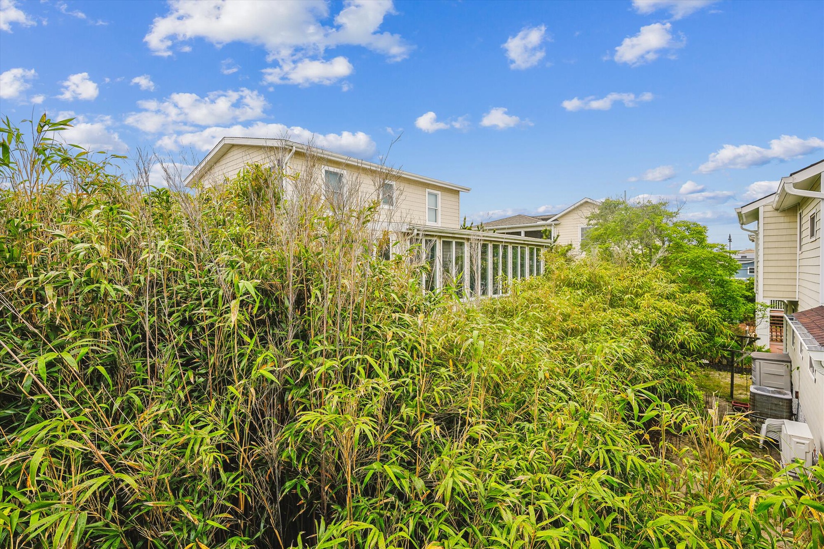 A residential property nestled within a lush, quiet neighborhood, surrounded by mature landscaping and neighboring homes under a bright, sunny sky.