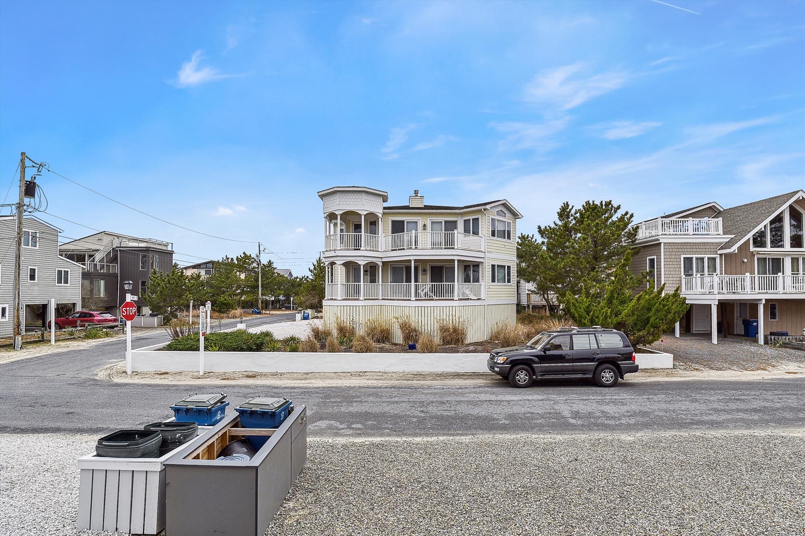 A charming two-story coastal property with wraparound balconies, surrounded by neighboring beach homes and natural landscaping in a peaceful residential area.