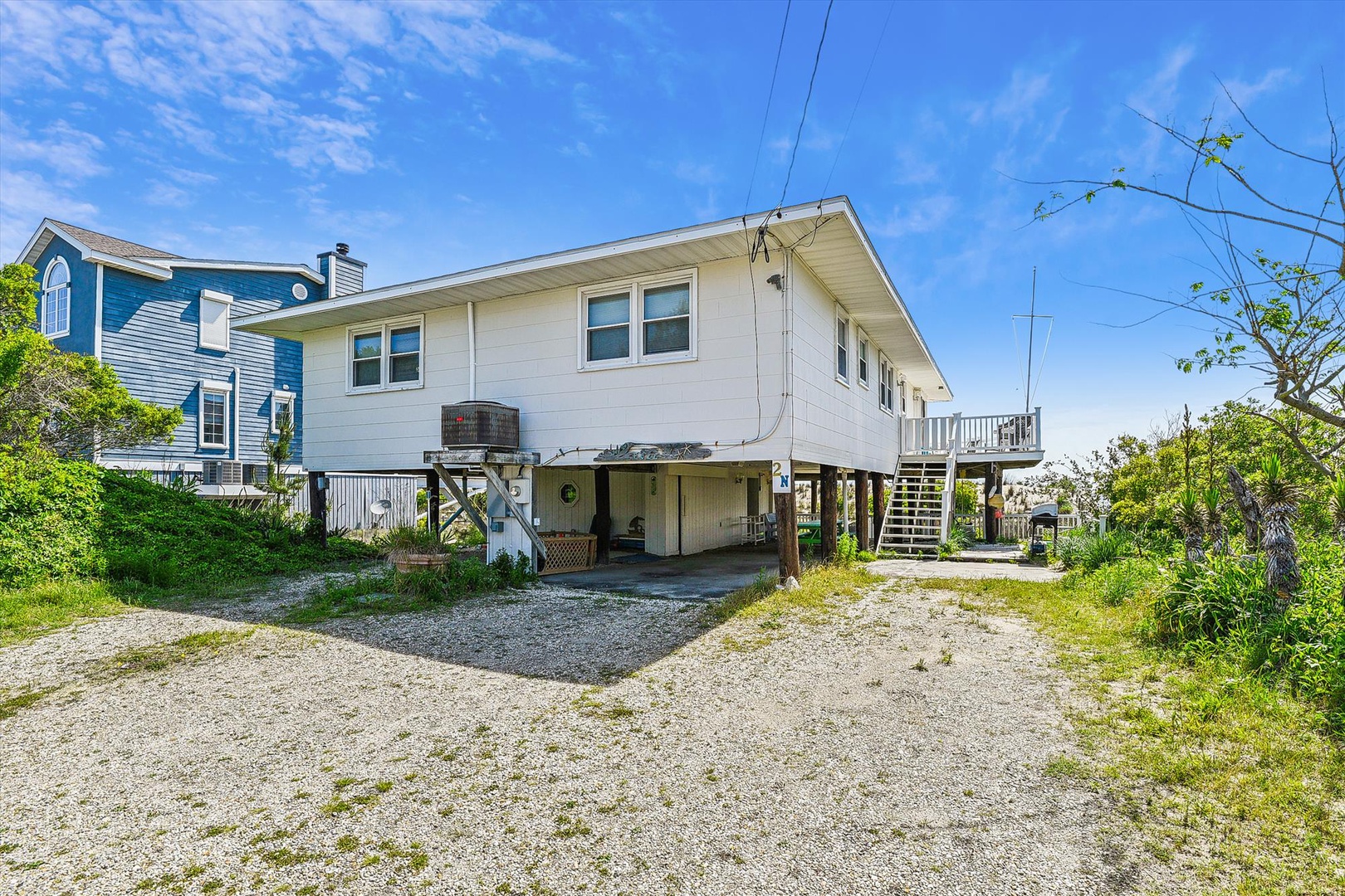A coastal home on stilts with ground-level parking, featuring a covered outdoor area and a quiet residential setting under sunny skies.