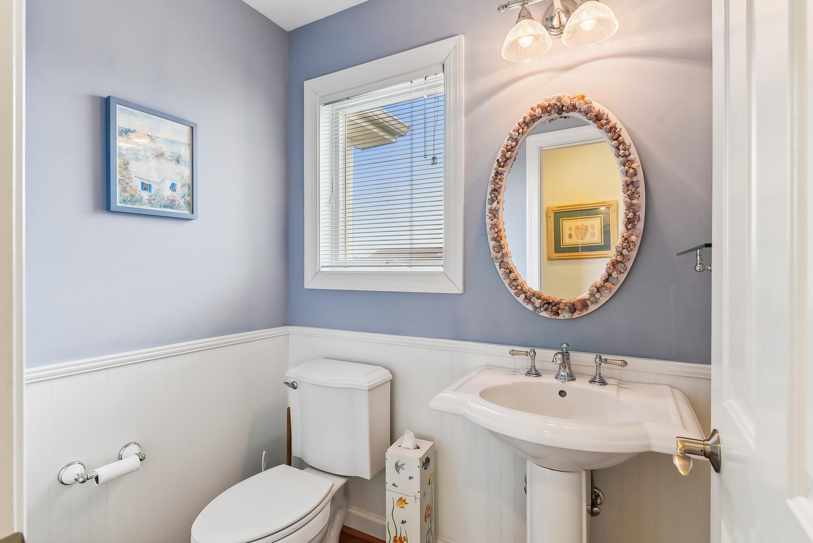 Freshen up in your coastal-inspired powder room with soft blue walls and a charming shell-framed mirror that brings beach vibes right inside.